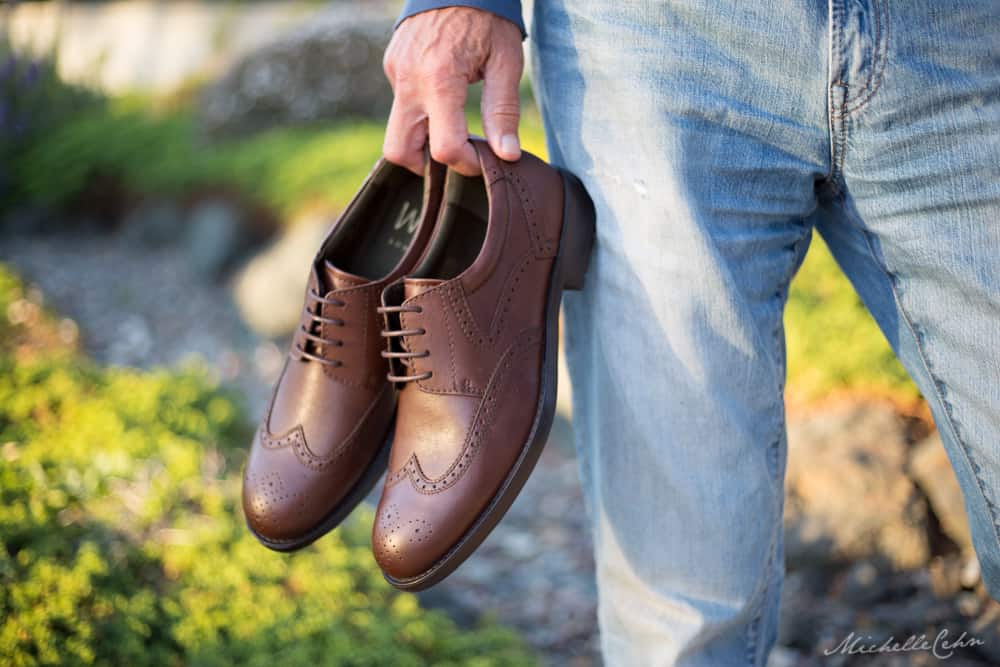 Man holding a pair of brown Will vegan shoes. 