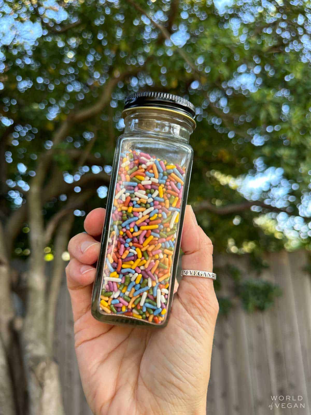 A glass container filled with rainbow vegan sprinkles from the brand Wilton.
