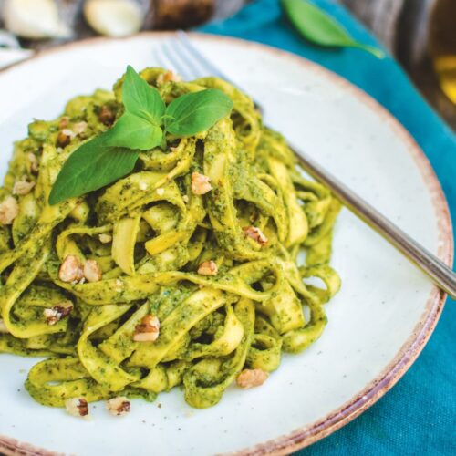 Close up of a neutral dish of vegan walnut pesto pasta with some decorative basil